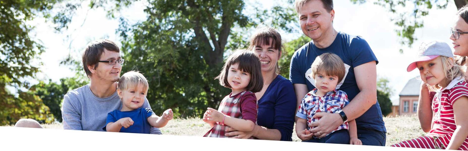 Kinder sitzen mit ihren Eltern auf dem Rasen und lachen